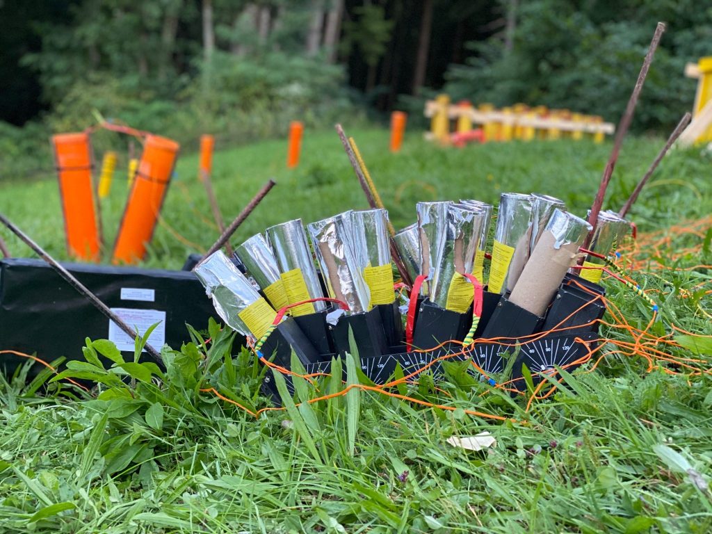 Verkabelte pyrotechnische Effekte in Abschussgestellen auf einer Wiese vor dem Feuerwerk.