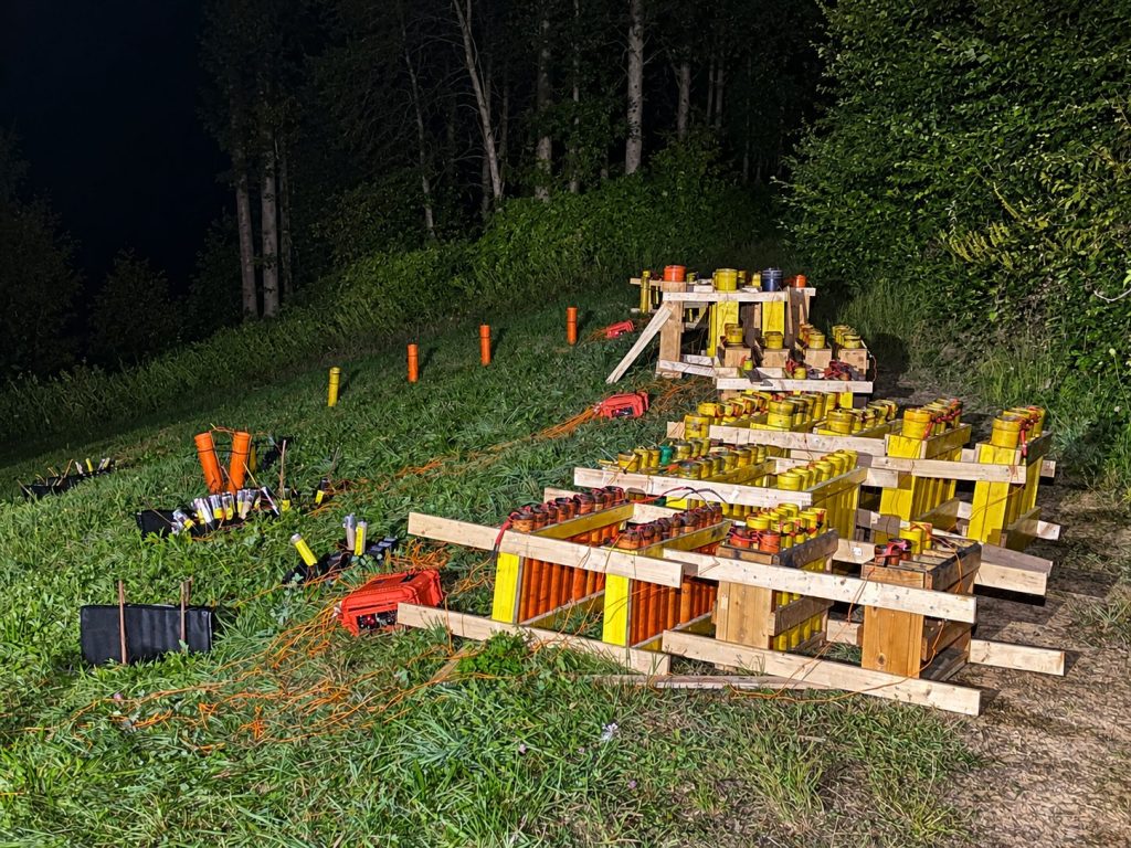 Aufgebautes und verkabeltes Feuerwerk mit Abschussgestellen auf einer Wiese bei Nacht.
