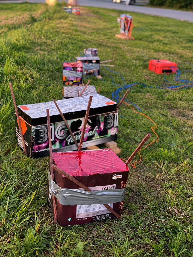 Gesicherte Feuerwerksbatterien mit Verkabelung auf einer Wiese während des Aufbaus.