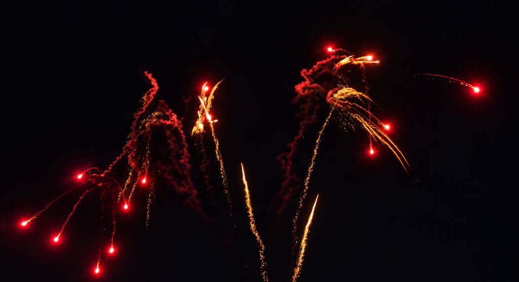 Rote und goldene Feuerwerkseffekte am nächtlichen Himmel.