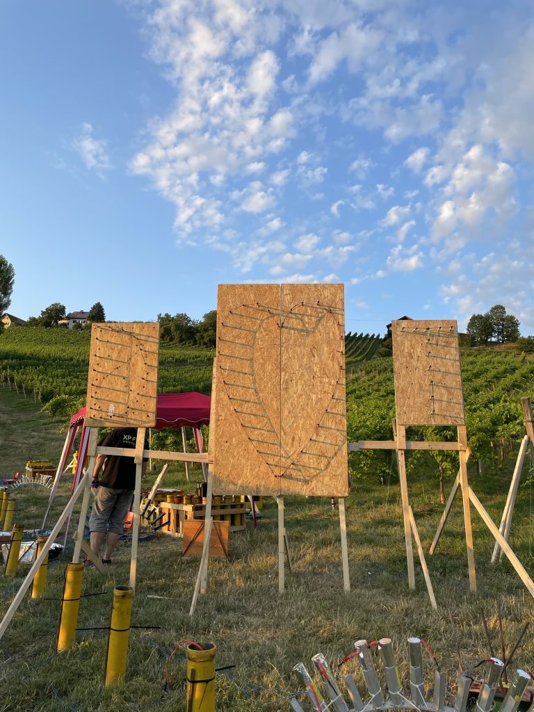Herzförmige Lichterbild-Installation mit drei pyrotechnischen Effekten vor südsteirischer Landschaft.