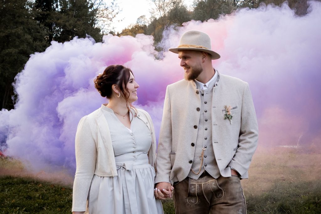 Brautpaar vor violetten und rosafarbenen Raucheffekten bei einer Hochzeit.