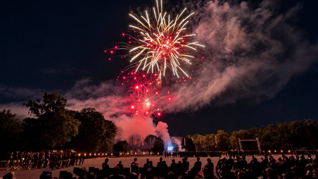 Rot-weißes Großfeuerwerk über einer Veranstaltung mit Zuschauern bei Nacht.