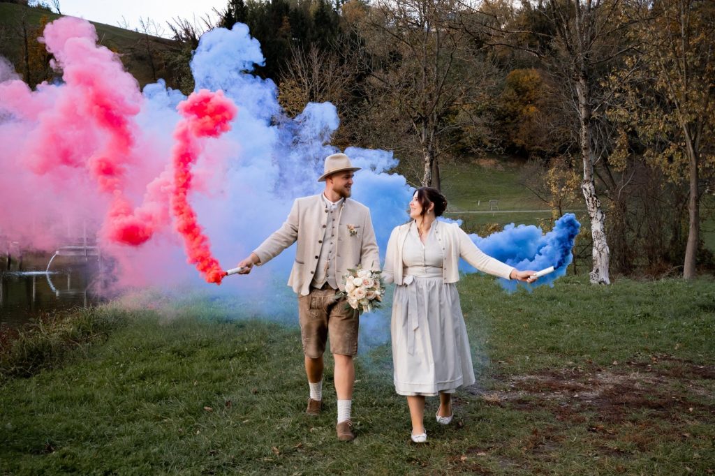 Brautpaar mit roten und blauen Raucheffekten bei einer Hochzeit im Freien.
