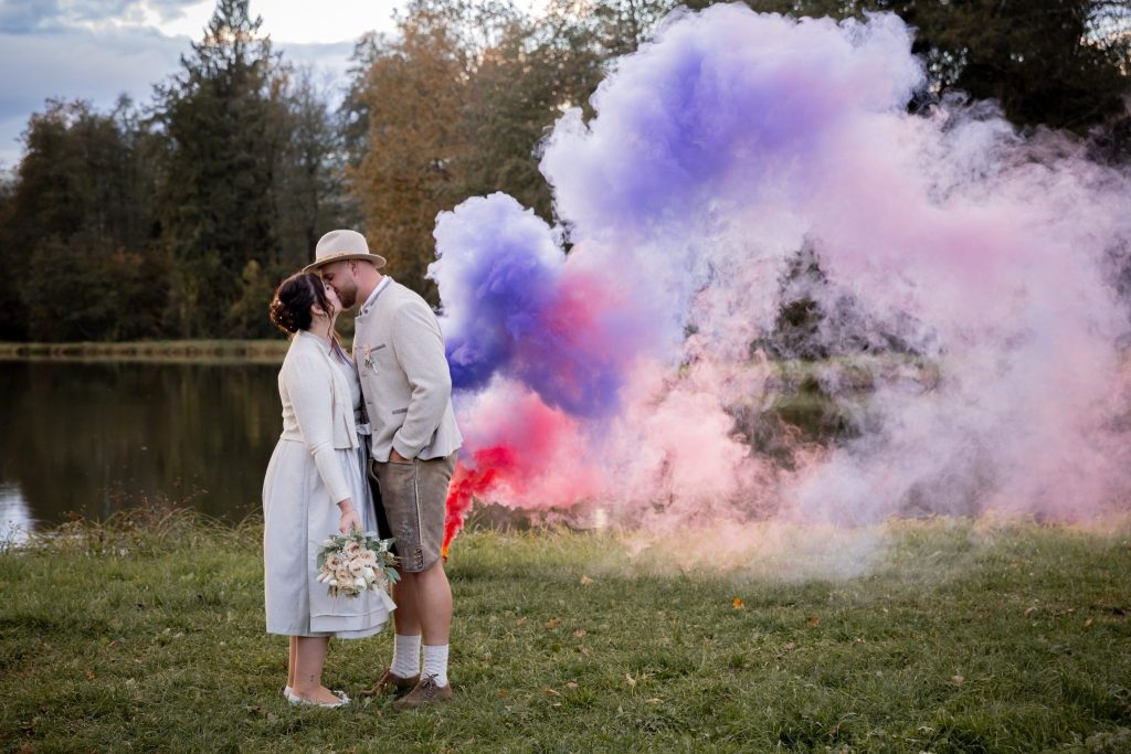 Brautpaar vor farbigem Rauch in Rosa und Violett bei einer Hochzeit im Freien.