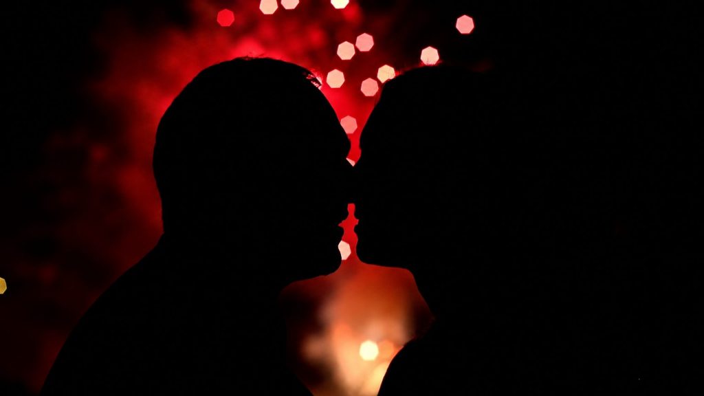 Silhouette eines küssenden Paares vor roten Lichtern bei einer romantischen Feuerwerksinszenierung.