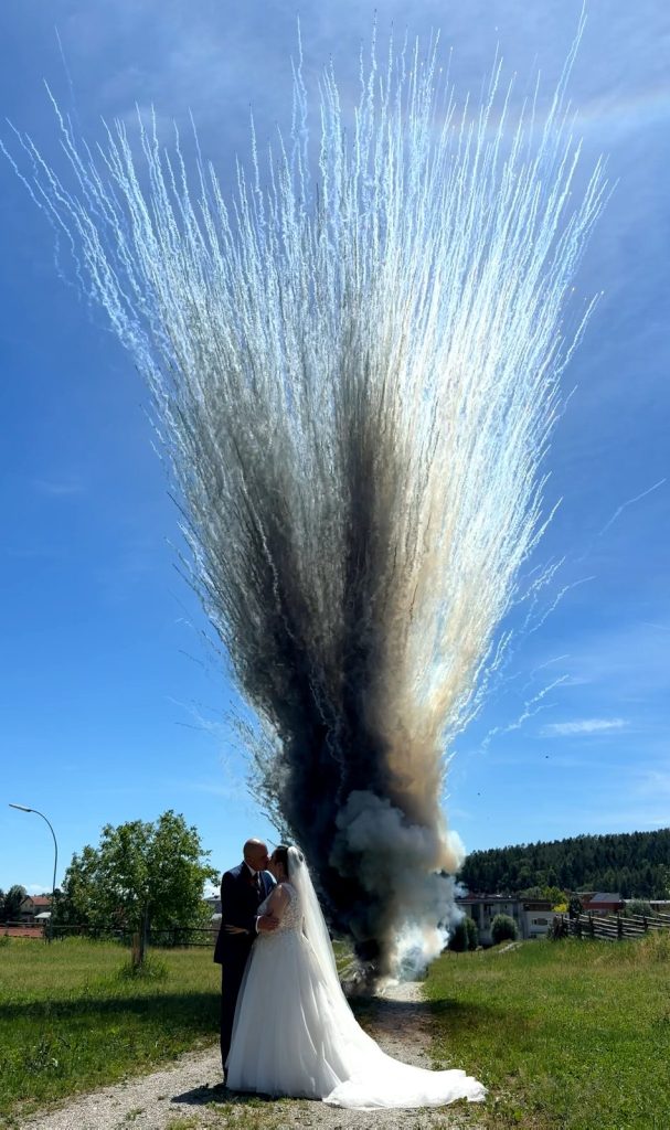 Brautpaar vor einem eindrucksvollen Tagesfeuerwerk mit weißen und schwarzen Raucheffekten.