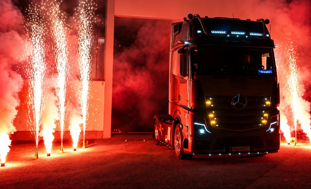 LKW zwischen hellen Fontänen und rotem Rauch